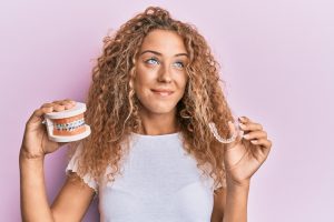 woman holding aligner and model of braces